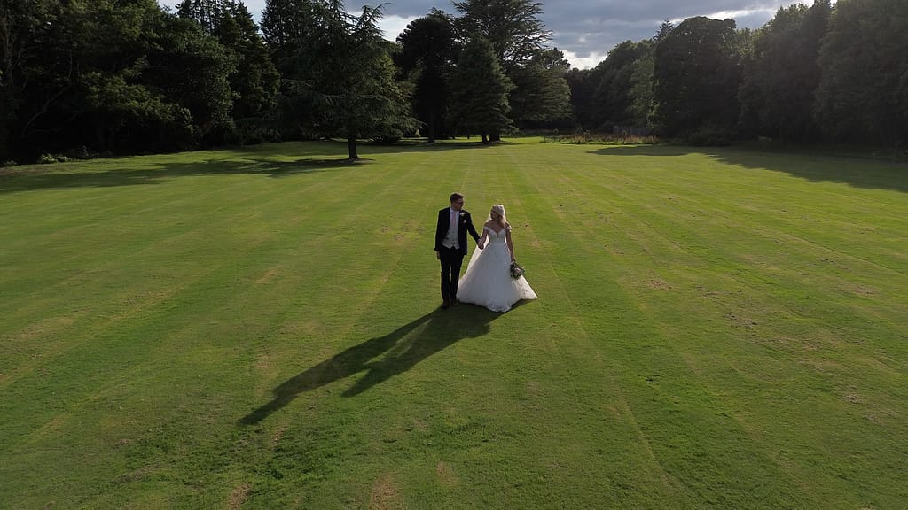 Bride and groom walking together across the lawn at Beamish Hall wedding venue, surrounded by historic architecture and greenery.