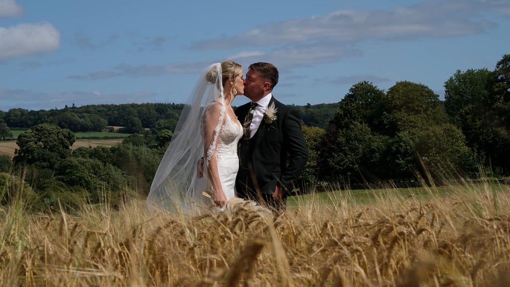 Bride and groom standing side by side in a golden cornfield at the Yorkshire Wedding Barn on their wedding day, smiling and holding hands amid the rural countryside. Yorkshire Wedding Barn Wedding Film
