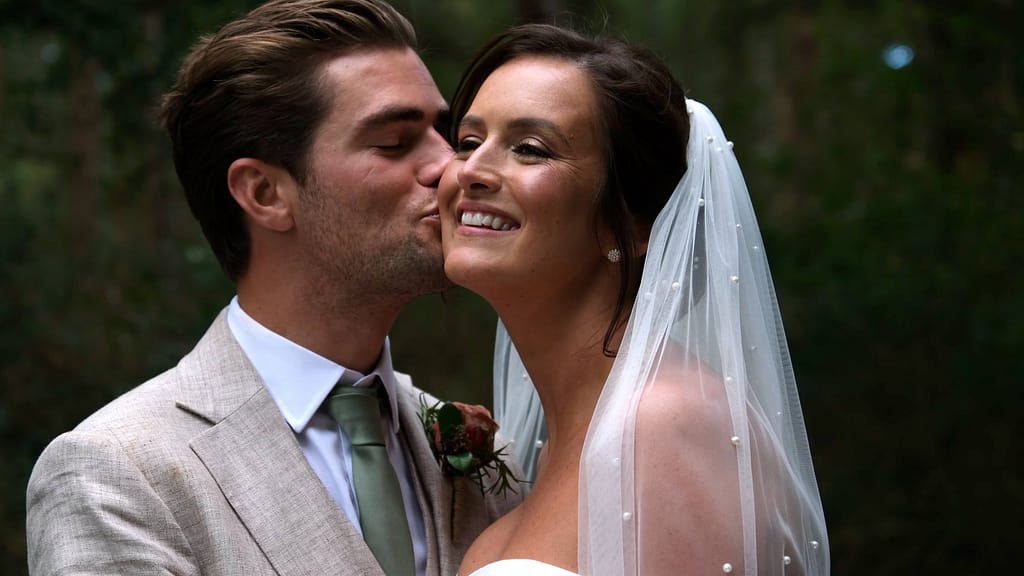 Ellie and Harry sharing a kiss at their Healey Barn Wedding as Ellie smiles in the sunshine